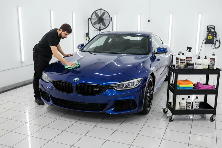 Detailer polishing blue BMW car in white garage with car care products and microfiber towels