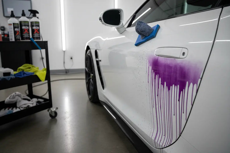 White sports car with purple iron remover on door panel during paint decontamination